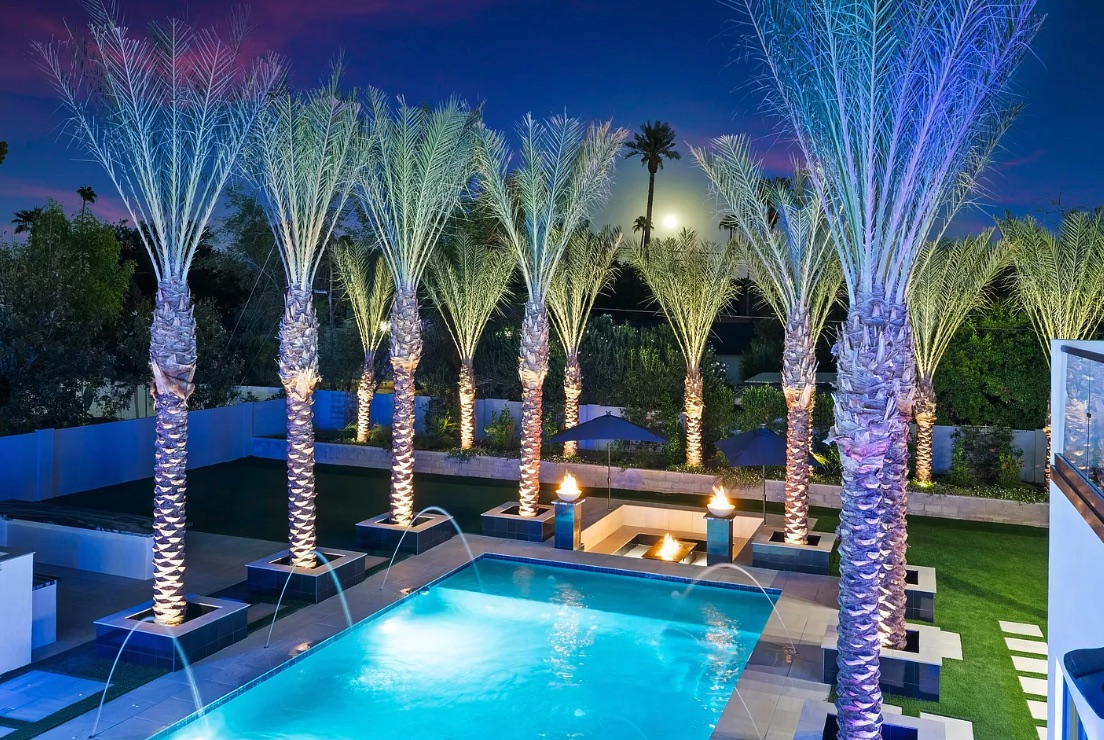 Twilight view of a palm-lined pool with fountain jets